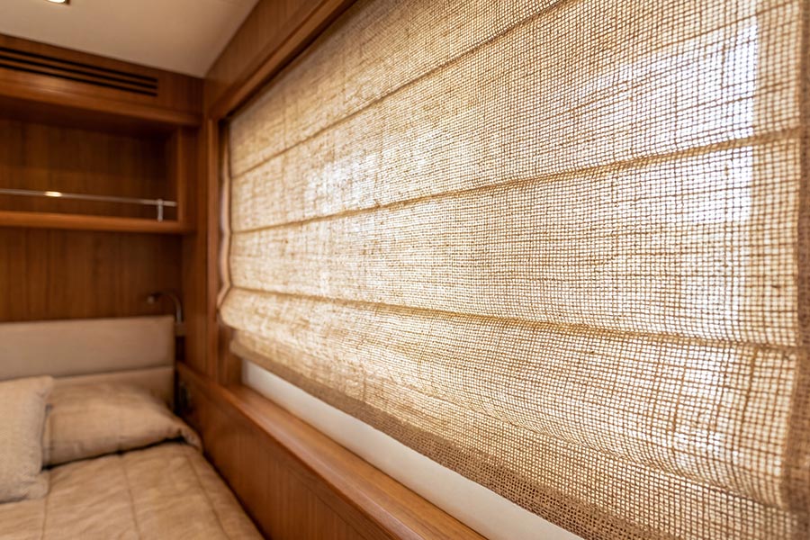 Woven burlap Roman shades covering a window in a wood-paneled boat bedroom